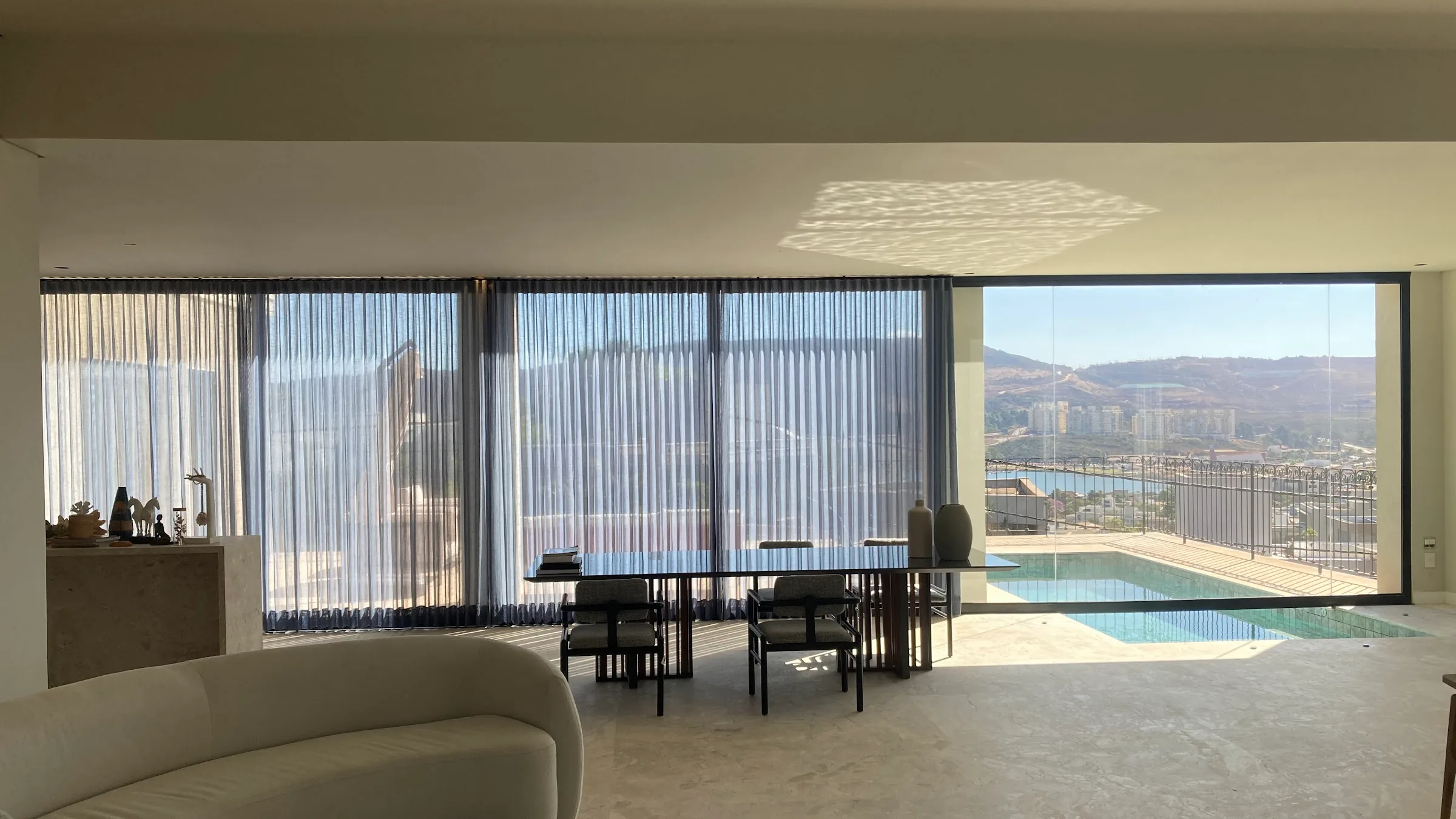 Ambiente de alto padrão com cortinas voil do piso ao teto e vista panorâmica, entregue pela Monteiro Interiores